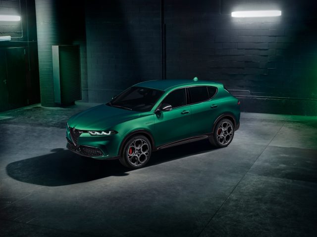 Een groene Alfa Romeo Tonale SUV staat binnen geparkeerd in een slecht verlichte kamer met betonnen vloeren en bakstenen muren. Twee fluorescentielampen erboven zorgen voor een subtiele verlichting van het gestroomlijnde voertuig.