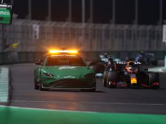 Een groene Aston Martin safety car leidt 's nachts de Formule 1-raceauto van Max Verstappen over een racecircuit.