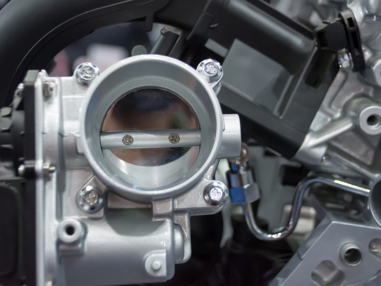 Close-up van een gasklephuisklep in een voertuigmotor, waarbij de metalen componenten en de aangesloten bedrading zichtbaar zijn, met duidelijk zicht op het gasklephuis voor betere prestaties.