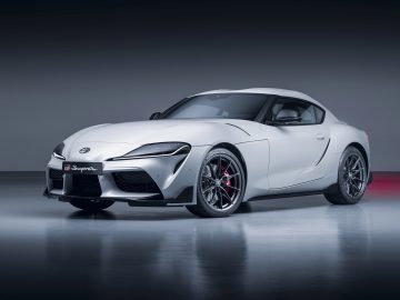 Een grijze GR Supra-sportwagen met een strak ontwerp, weergegeven tegen een effen grijze achtergrond. De auto heeft glanzende lichtmetalen velgen en een prominente grille.