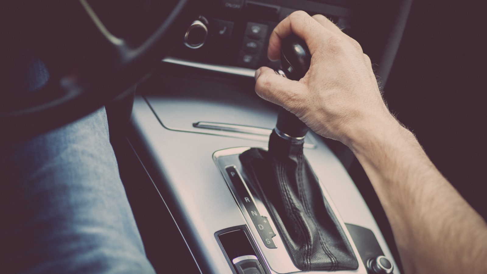 Close-up van iemands hand op de versnellingspook in een auto-interieur, met de versnellingspook in de neutrale stand. De afbeelding concentreert zich op de middenconsole en het schakelmechanisme en benadrukt de precisie die nodig is voor handelingen als het automaatspoelen.