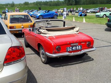 Een klassieke rode cabriolet van Honda, geparkeerd tussen andere vintage en moderne auto's op een openlucht auto-evenement, belichaamt echt de term Elk Merk Waardig. Kentekenplaat zichtbaar: DZ-41-88.