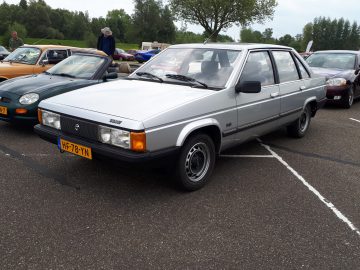 Een zilveren vierdeurs Talbot Solara-auto, geparkeerd op een parkeerplaats met andere voertuigen eromheen, valt op als echt elk merkwaardig. Op het gele kenteken staat 'HF-78-YN' en op de achtergrond zijn bomen en groen zichtbaar.