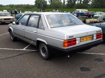 Een zilveren Talbot Tagora sedan met het gele Nederlandse kenteken "HF-78-YN" staat trots op een autoshow, omringd door andere oldtimers, die de geest van Elk Merk Waardig belichamen.