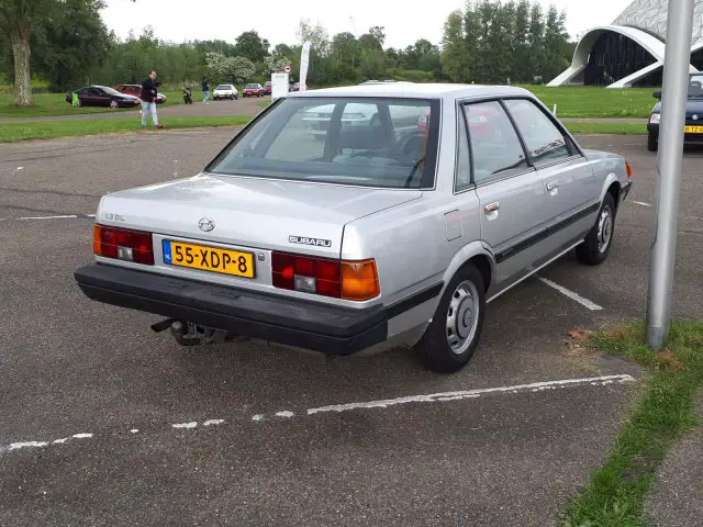 Zilveren Subaru sedan geparkeerd op een buitenterrein met groen gras en bomen op de achtergrond. De auto, Elk Merk Waardig, is voorzien van Nederlands kenteken.