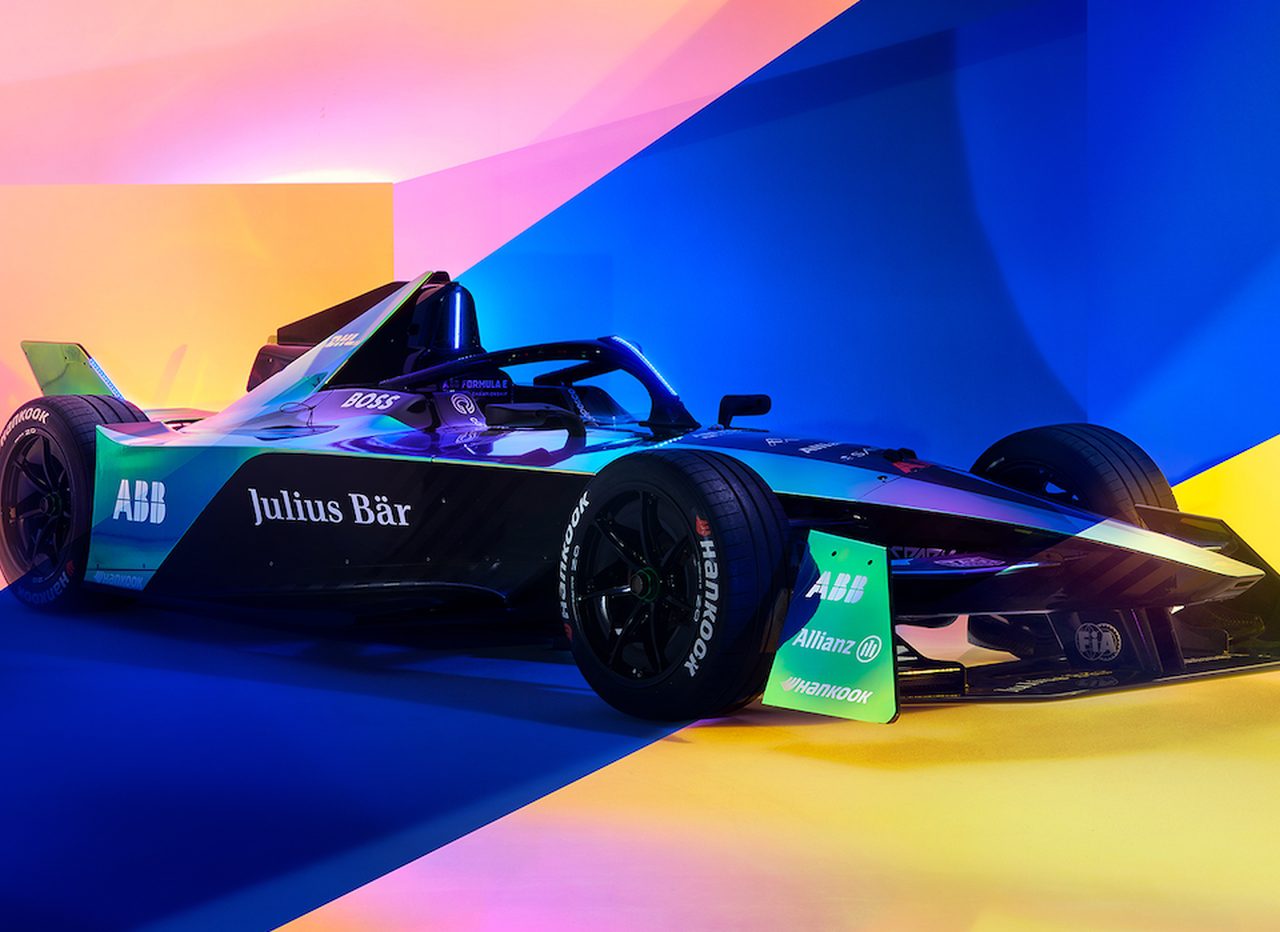 Een strakke elektrische racewagen wordt getoond tegen een kleurrijke achtergrond van blauw, roze en geel. De auto is voorzien van logo's van ABB, Julius Bär en Allianz, met een futuristisch ontwerp dat de geavanceerde geest van Formule E belichaamt.