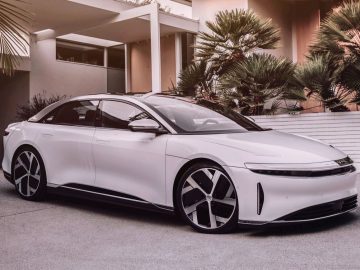 Een strakke, witte Lucid Air staat geparkeerd op een oprit voor een modern huis met tropische tuin.