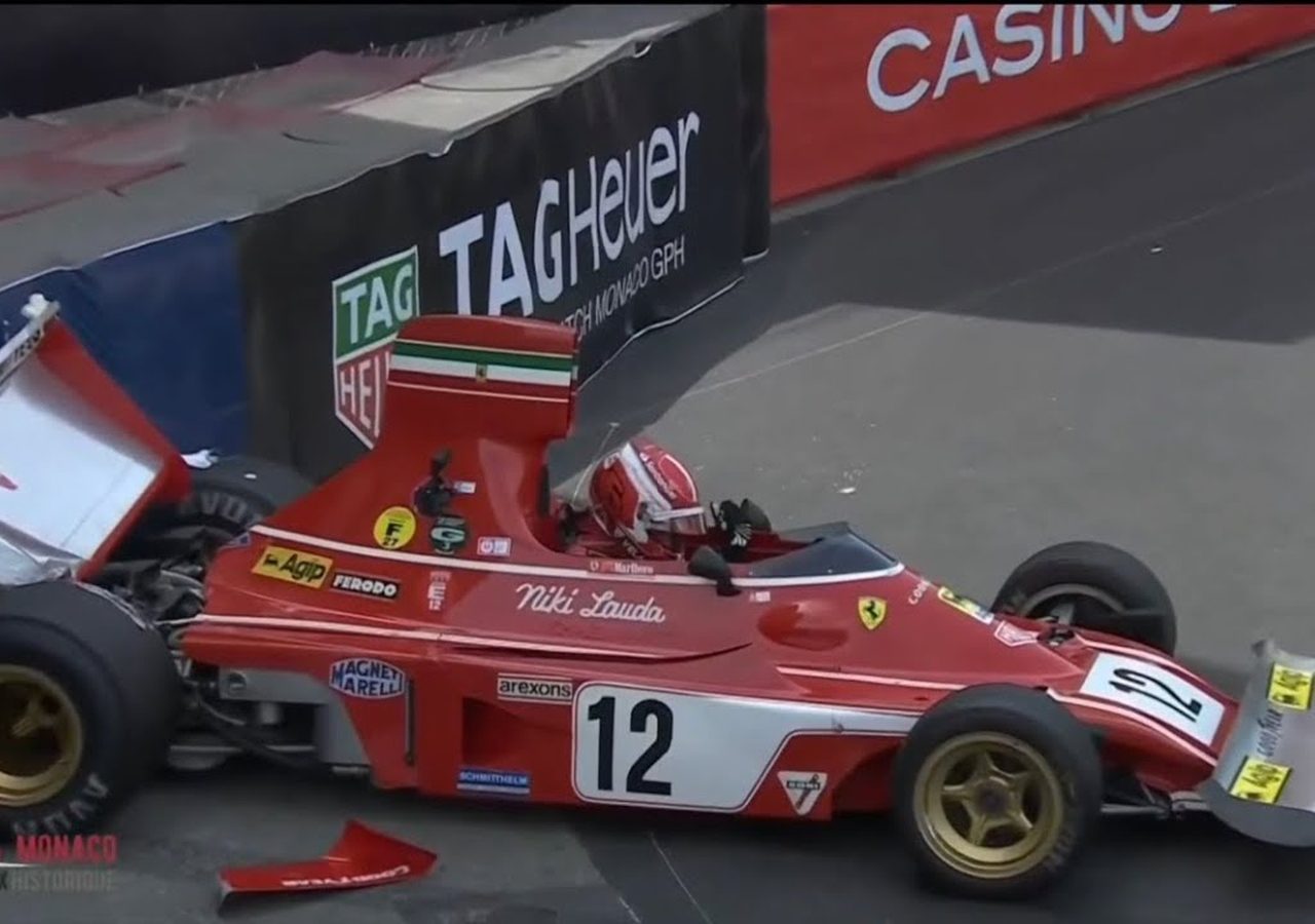 Een rode Formule 1-auto met het nummer 12 botst tijdens een race tegen een barrière, met zichtbare schade aan de achtervleugel. Charles Leclerc zit nog in het voertuig.
