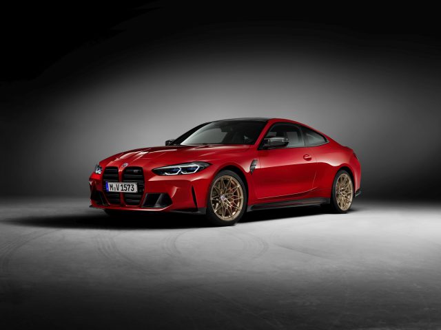 Een rode BMW M sportwagen met een strak design en zwarte accenten, binnen geparkeerd op een grijze vloer. Het voertuig is voorzien van gouden wielen en een tweedeurs coupé carrosserievorm.