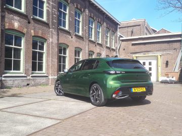 Voor een bakstenen gebouw met meerdere ramen staat een Peugeot 308 geparkeerd. De achterste kentekenplaat van de groene auto is zichtbaar.