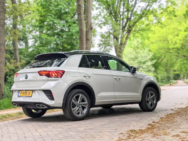 Een witte Volkswagen T-Roc geparkeerd op een stenen weg in een bosrijke omgeving op een zonnige dag, wat het strakke ontwerp laat zien. Lees onze recensie van de Volkswagen T-Roc om meer te ontdekken over zijn indrukwekkende kenmerken en prestaties.