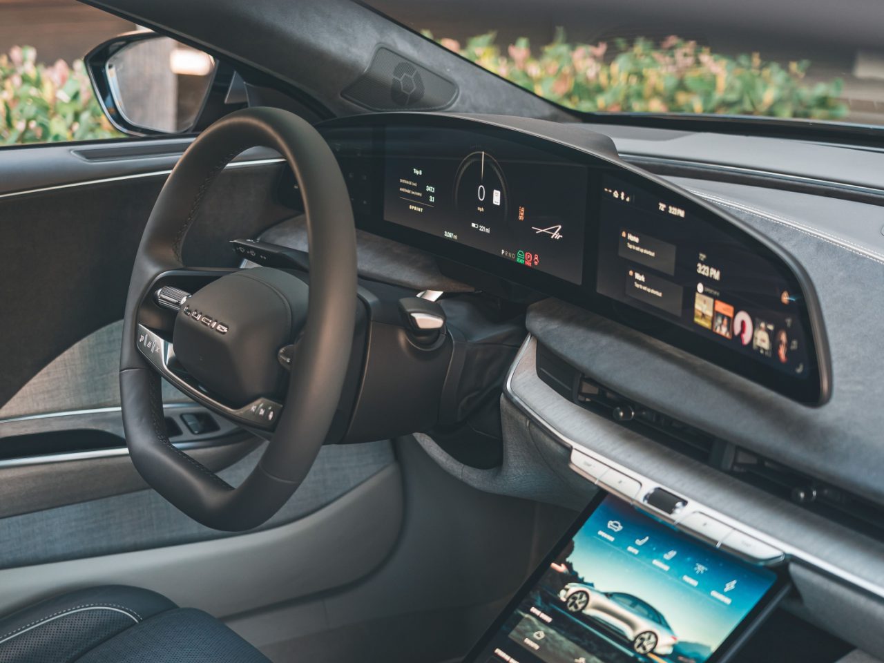 Een auto-interieur met een strak dashboard met digitaal display, een groot touchscreen middenconsole en een stuurwiel versierd met het Porsche-logo, dat doet denken aan de moderne verfijning van de Lucid Air.