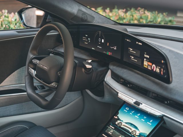 Een auto-interieur met een strak dashboard met digitaal display, een groot touchscreen middenconsole en een stuurwiel versierd met het Porsche-logo, dat doet denken aan de moderne verfijning van de Lucid Air.