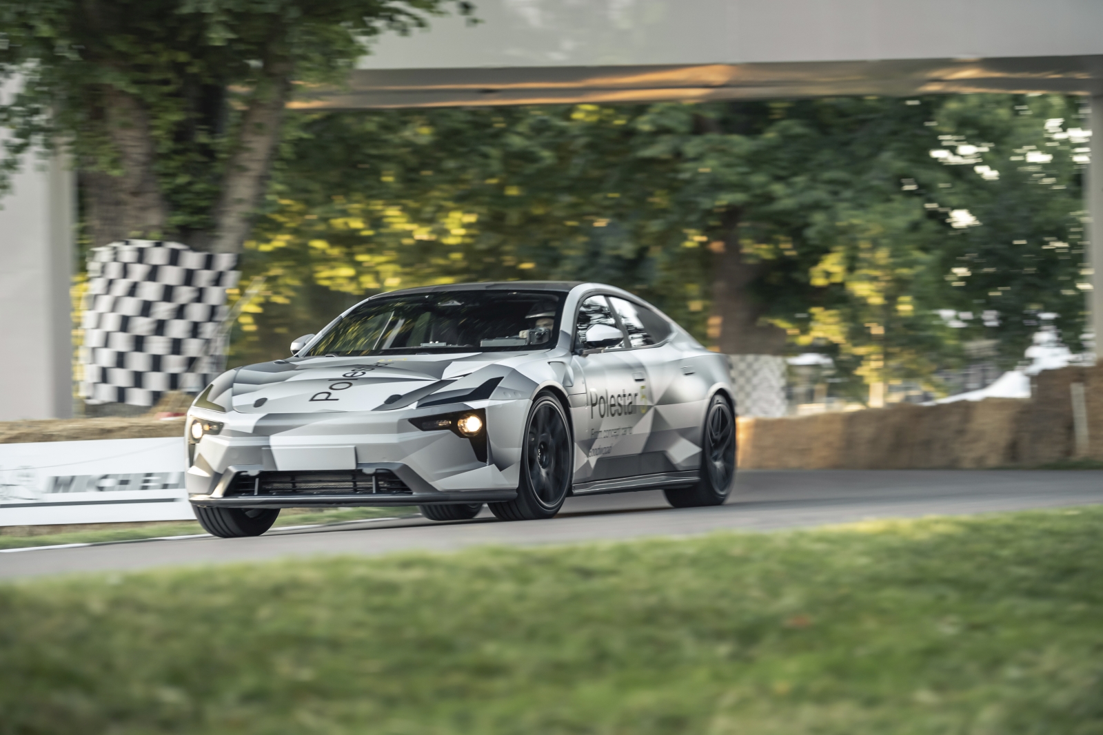 Een strakke Polestar 5 rijdt over een circuit met hooibalen op de achtergrond, omgeven door groen en geblokte vlaggen.