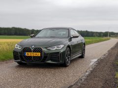 Een donkergroene BMW M440i Gran Coupé met kenteken N-373-HJ staat op een bewolkte dag geparkeerd op een smalle verharde weg, met grasvelden en bomen op de achtergrond.