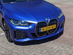 Close-up van de voorkant van een blauwe BMW i4 met een Nederlands kenteken met de tekst 'N-370-NT', geparkeerd op een geplaveid oppervlak.