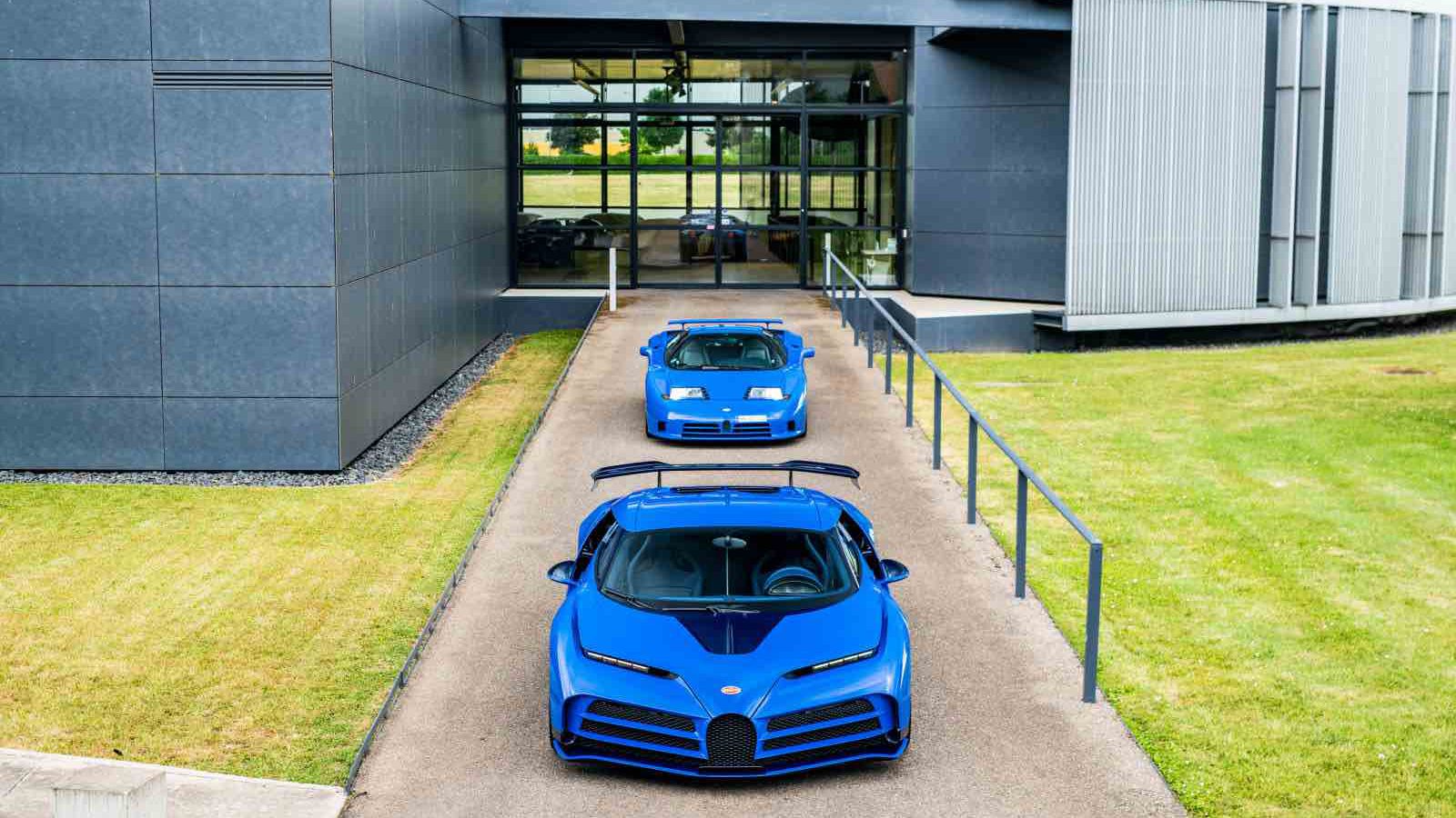 Twee blauwe sportwagens staan geparkeerd voor een modern gebouw met grote ramen en grijze buitenmuren. Zien: dit is de eerste klantgeleverde Bugatti Centodieci, die een vleugje exclusiviteit aan de scène toevoegt.