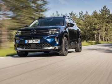 Een zwarte Citroën C5 Aircross SUV rijdt over een landelijke weg, met vage bomen op de achtergrond.