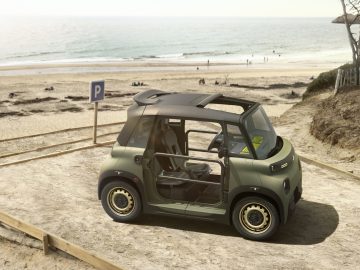 Een kleine, groene Citroen Ami staat op een zonnige dag geparkeerd vlakbij een zandstrand met de oceaan op de achtergrond.