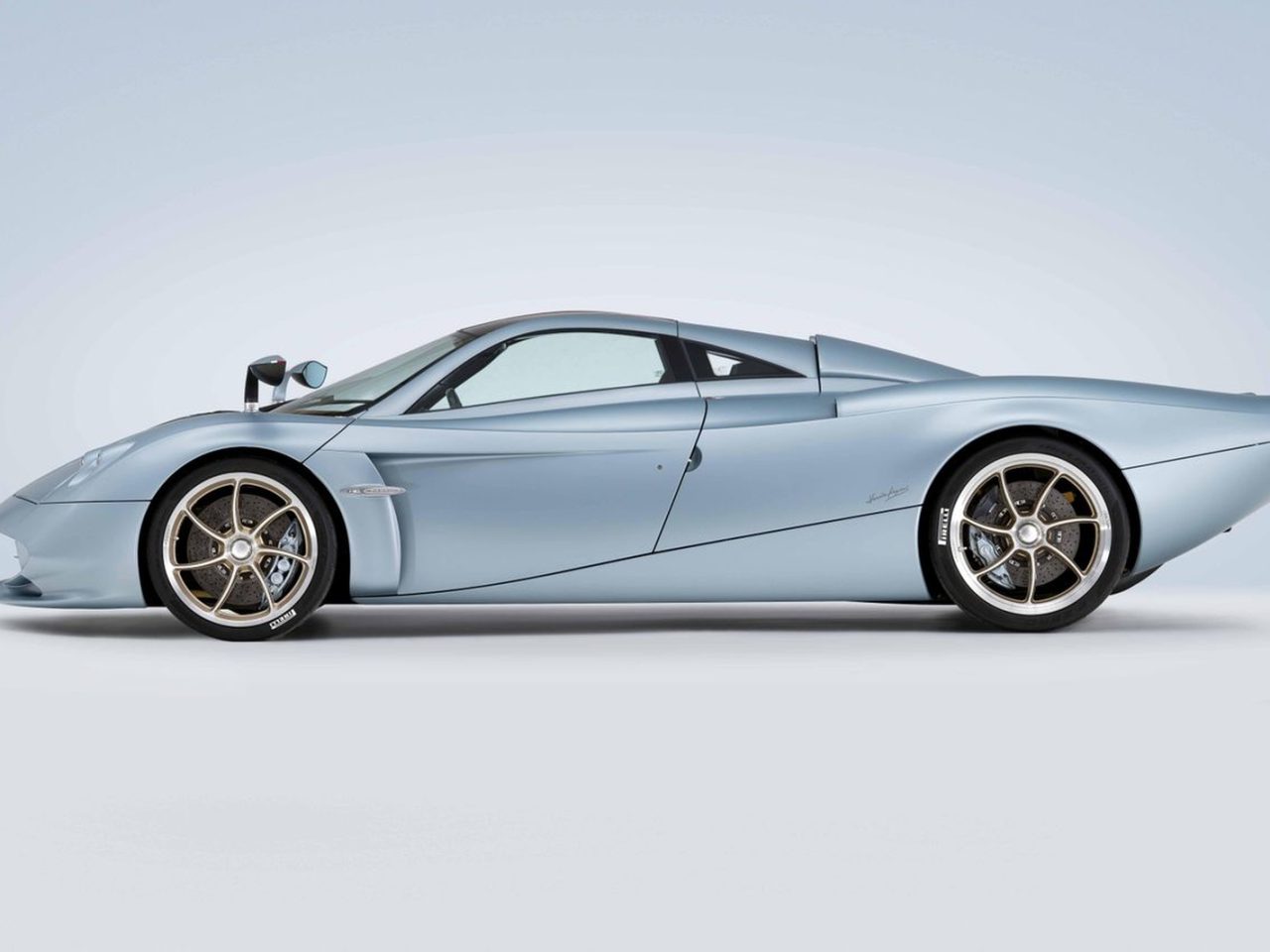 Een slanke, metallic zilveren Pagani-sportwagen met een aerodynamisch ontwerp, laag profiel en zichtbare lichtmetalen velgen, gezien vanaf de zijkant op een eenvoudige lichtgrijze achtergrond.