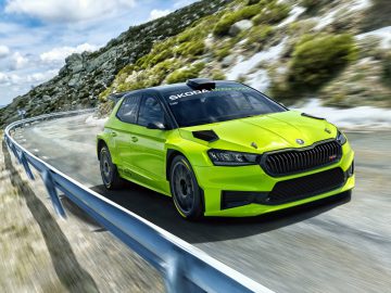 Een felgroene Škoda Fabia-racewagen rijdt snel over een bergachtige weg met een metalen vangrail onder een blauwe lucht met wolken.