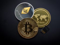 Een zilveren Ethereum-munt, een gouden Ripple-munt en een gouden Bitcoin-munt zijn gerangschikt op een donkere achtergrond naast een kleine geheugenkaart, die de ins en outs van crypto vertegenwoordigt en hoe je geld kunt verdienen in dit digitale landschap.