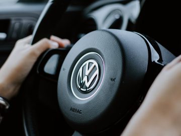 Close-up van de handen van een persoon op het stuur van een Volkswagen-auto, met het Volkswagen-logo prominent in het midden, wat een gevoel van betrouwbaarheid uitstraalt dat vaak wordt geassocieerd met hun privélease-opties.
