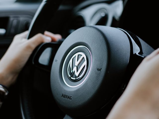Close-up van de handen van een persoon op het stuur van een Volkswagen-auto, met het Volkswagen-logo prominent in het midden, wat een gevoel van betrouwbaarheid uitstraalt dat vaak wordt geassocieerd met hun privélease-opties.