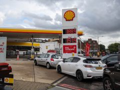 Auto's staan in de rij bij een Shell-tankstation met brandstofprijzen van 188,9 voor loodvrij en 179,9 voor diesel, wat doet denken aan de tarieven voor tanken in Duitsland. Boven het station is een bewolkte hemel zichtbaar.