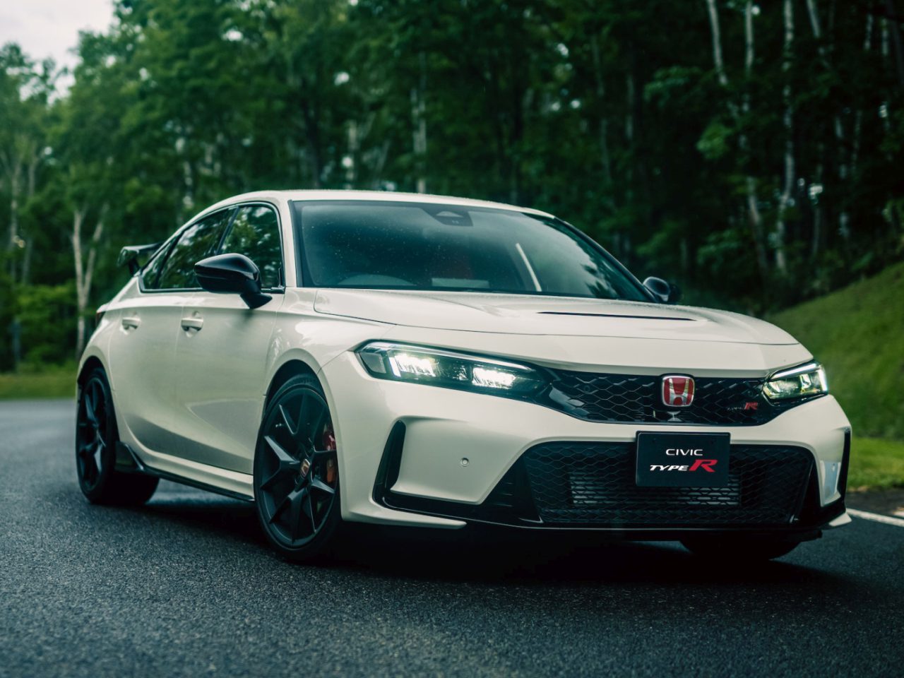 Een smetteloos witte Honda Civic Type R staat geparkeerd op een bochtige weg, waarbij het strakke ontwerp contrasteert met de weelderige bosachtergrond.