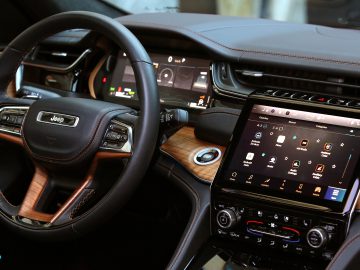 Binnenaanzicht van een modern Jeep Grand Cherokee-dashboard met een stuurwiel met bedieningselementen, digitale displays en een infotainment-touchscreen met verschillende apps.