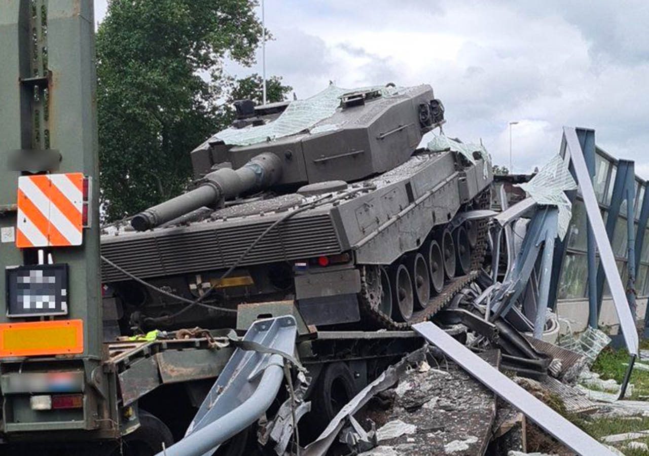 Een tank is tegen een brug gebotst en heeft aanzienlijke structurele schade aan zowel de brug als zichzelf veroorzaakt. Puin en verwrongen metaal liggen verspreid over het toneel, waardoor een chaotisch spektakel ontstaat.