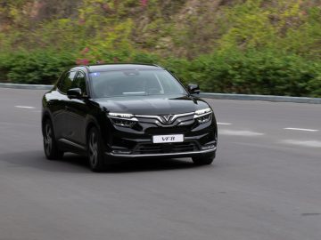 Een VinFast VF8 elektrische SUV rijdt over een verharde weg met weelderig groen op de achtergrond.