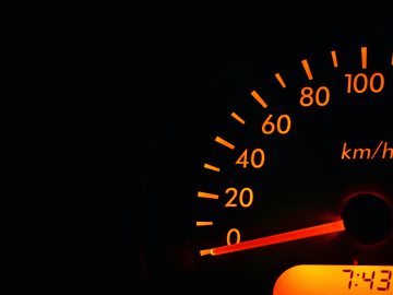Close-up van de snelheidsmeter van een auto met een snelheid van ongeveer 10 km/u, met een digitale klok die 7:43 uur weergeeft. Houd er rekening mee dat de verzekeringstarieven aanzienlijk kunnen stijgen na te hard rijden.