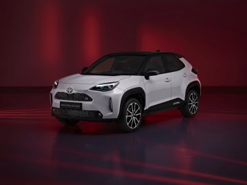 Een witte Toyota Yaris Cross GR Sport SUV tentoongesteld in een studio met rode verlichting, met een schuin vooraanzicht.