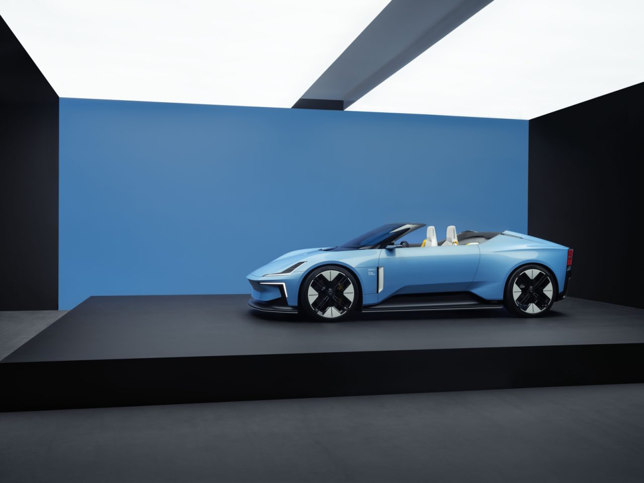 De Polestar 6, een blauwe, moderne cabriolet, staat tentoongesteld in een minimalistische ruimte met een blauwe muur en witte plafondpanelen erboven.