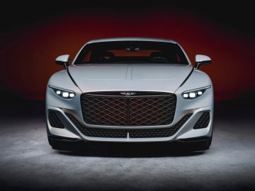 Vooraanzicht van een witte luxe sportwagen van Bentley met verlichte koplampen en een prominente grille, tegen een donkere achtergrond met kleurovergang.