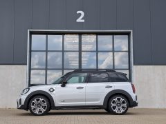 Een witte Mini Countryman parkeerde voor een groot, grijs industrieel gebouw met een nummer 2 boven de deuropening. De reflecterende ramen van het gebouw laten een gedeeltelijk bewolkte hemel zien.