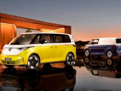 Twee Volkswagen ID. Buzz-voertuigen worden in de schemering buiten tentoongesteld. De voorste Volkswagen ID. Buzz heeft een geel-witte buitenkant, terwijl het achterste voertuig een blauw-witte buitenkant heeft.
