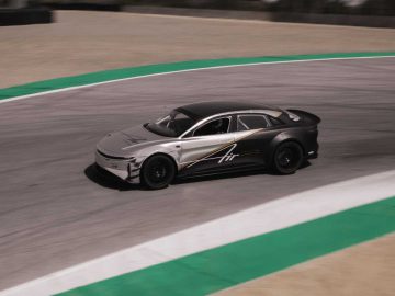 Een zilver-zwarte sportwagen met de tekst 'Lucid Air' op de zijkant rijdt op een verharde racebaan met groen en rood geverfde stoepranden.