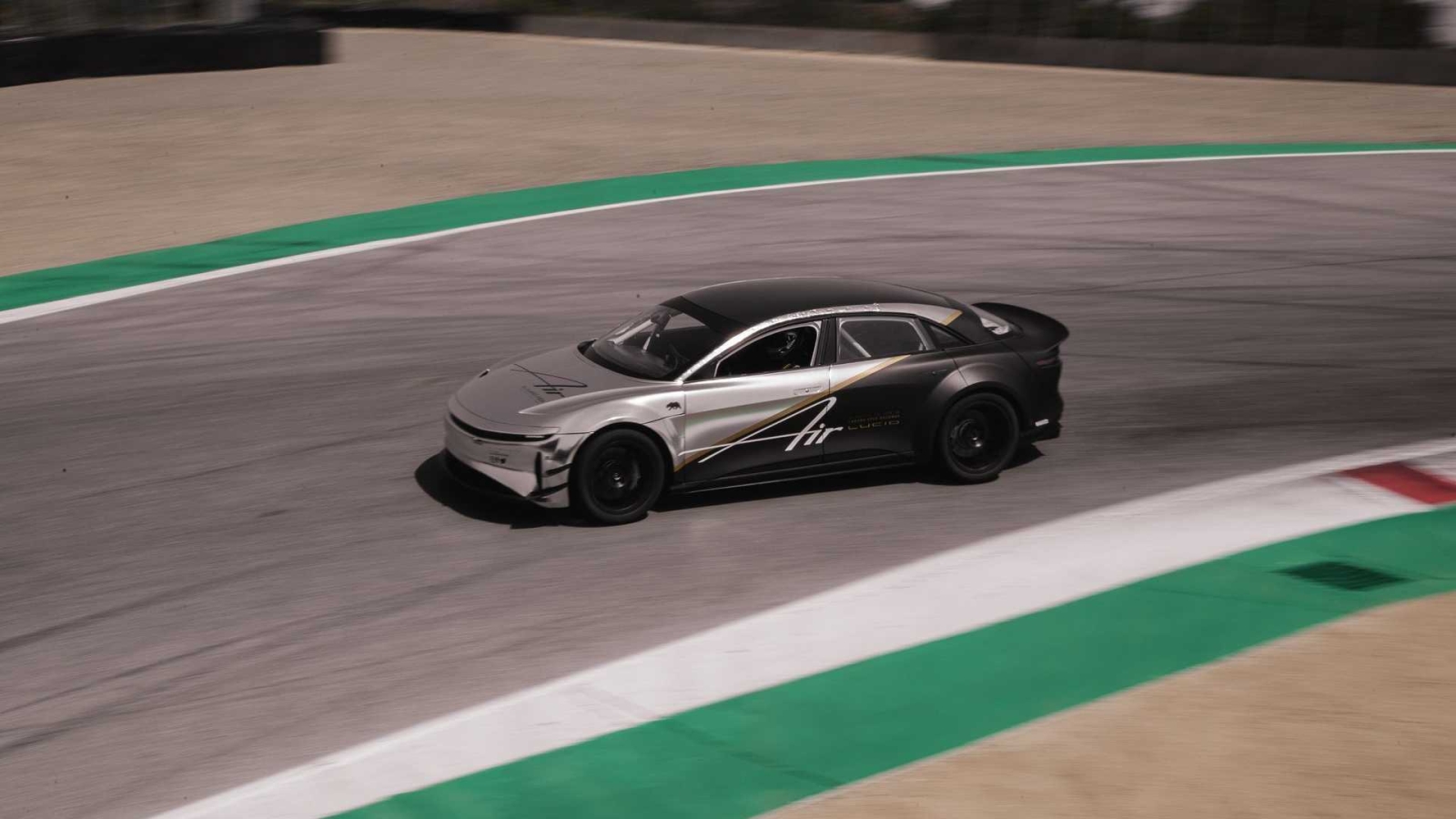 Een zilver-zwarte sportwagen met de tekst 'Lucid Air' op de zijkant rijdt op een verharde racebaan met groen en rood geverfde stoepranden.