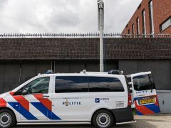 Voor een bakstenen gebouw staat een Nederlands politiebusje met de opschriften