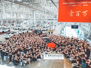 Een grote groep mensen in bijpassende zwarte shirts viert feest rond een rode Tesla in een fabrieksomgeving, met een spandoek met de tekst "1 Million" voor de auto geplaatst.