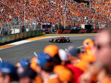 Een Formule 1-auto rijdt de bocht om op het circuit van Zandvoort, nauwlettend in de gaten gehouden door een grote menigte toeschouwers in oranje shirts.