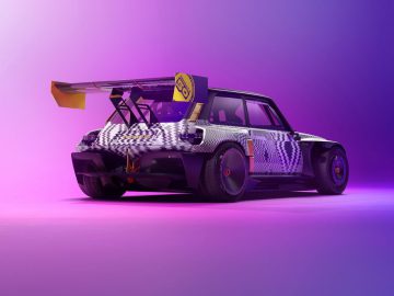 Een aangepaste Renault R5 Turbo 3E compacte auto met een grote achtervleugel en kleurrijke geometrische wrap staat geparkeerd op een roze en paars verlichte achtergrond.