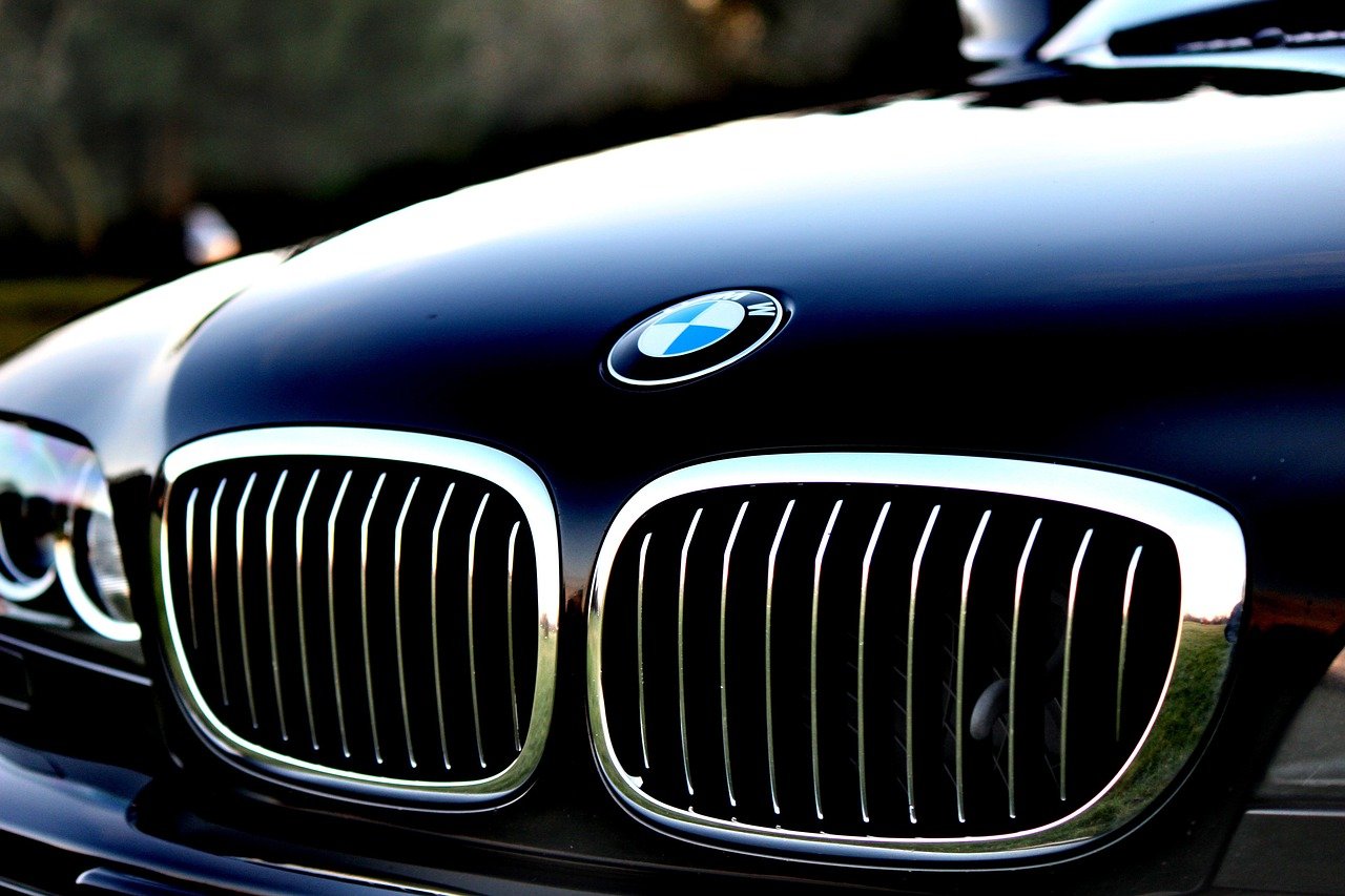 Close-up van de grille en het embleem van een zwarte BMW-auto. De auto is voorzien van de kenmerkende niervormige grilles en een glanzende afwerking, die de voordelen van investeren in luxe laat zien, zowel nieuw als tweedehands.
