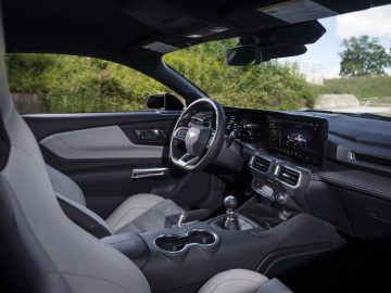 Binnenaanzicht van een moderne auto met zwarte en grijze stoelen, een centraal touchscreen, een stuur en een handgeschakelde versnellingsbak. Ford presenteert de gloednieuwe Mustang, die een strak design combineert met geavanceerde technologie.