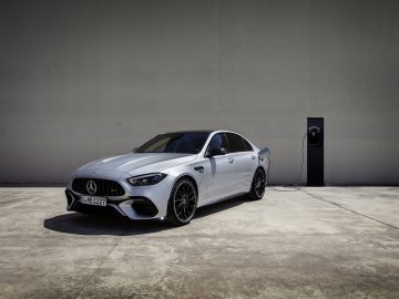 Een strakke Mercedes-AMG C 63 S E Performance sedan staat tijdens het opladen geparkeerd bij een laadstation op een lege betonnen parkeerplaats.