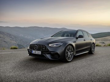 Een matzwarte Mercedes-AMG C 63 S E Performance stationwagen staat geparkeerd op een weg met bergen en een pastelkleurige lucht op de achtergrond.