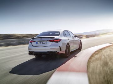 Een witte Mercedes-AMG C 63 S E Performance sedan rijdt op een racecircuit, van achteren gezien, terwijl hij op een zonnige dag een bocht navigeert.